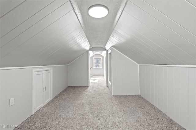 additional living space featuring light colored carpet, wooden walls, and vaulted ceiling