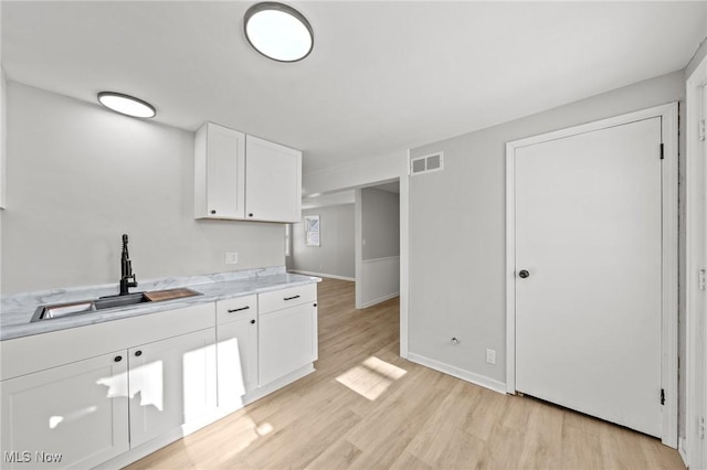 kitchen with sink, light wood-type flooring, white cabinetry, and light stone counters