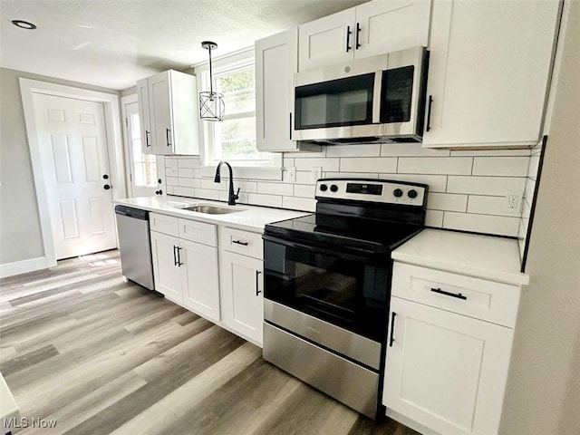 kitchen with decorative light fixtures, sink, light wood-type flooring, white cabinetry, and stainless steel appliances