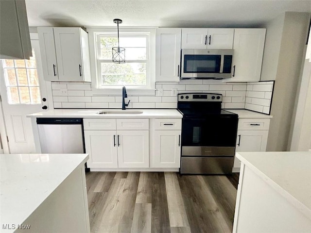 kitchen featuring light hardwood / wood-style floors, white cabinetry, sink, pendant lighting, and stainless steel appliances