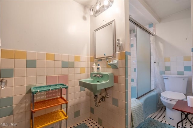 full bathroom with tile patterned flooring, sink, tile walls, toilet, and combined bath / shower with glass door