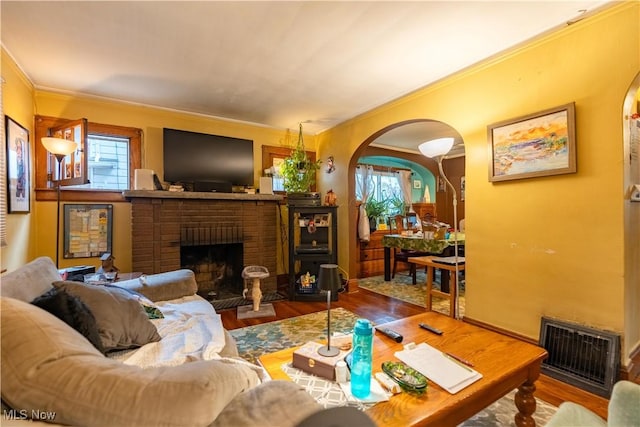 living room with wood-type flooring, ornamental molding, and a fireplace