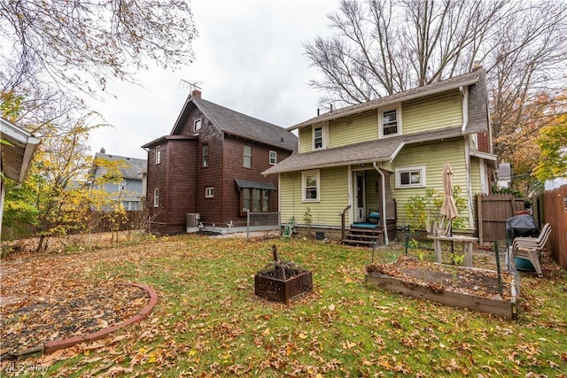 rear view of property featuring a lawn, central AC, and a fire pit