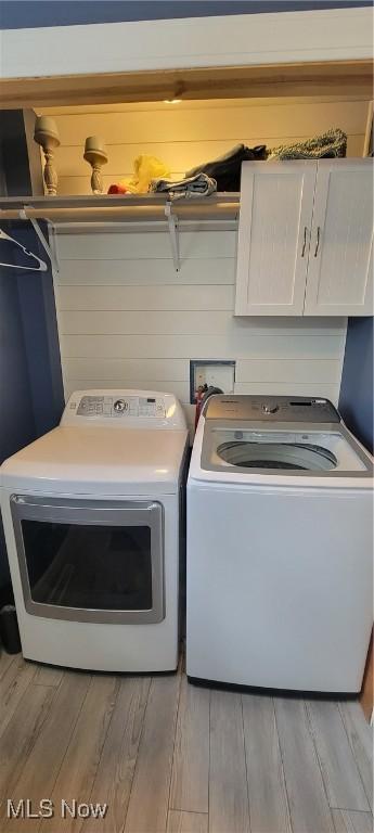 washroom featuring washing machine and dryer, cabinet space, and wood finished floors