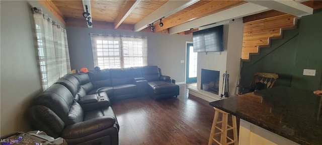 living area with dark wood-style flooring, beam ceiling, stairway, a brick fireplace, and wooden ceiling