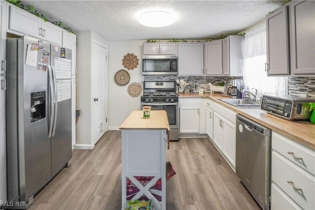 kitchen with a textured ceiling, a center island, stainless steel appliances, sink, and butcher block countertops