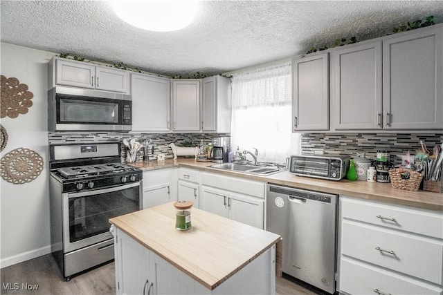 kitchen with appliances with stainless steel finishes, a textured ceiling, sink, a kitchen island, and light wood-type flooring