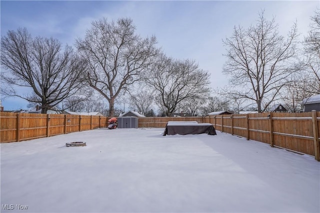 yard layered in snow featuring a storage shed and a fire pit