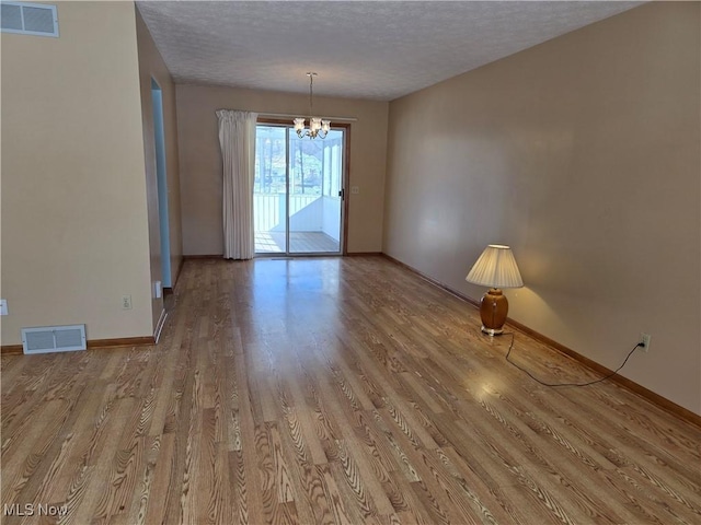 spare room with a notable chandelier, light hardwood / wood-style flooring, and a textured ceiling