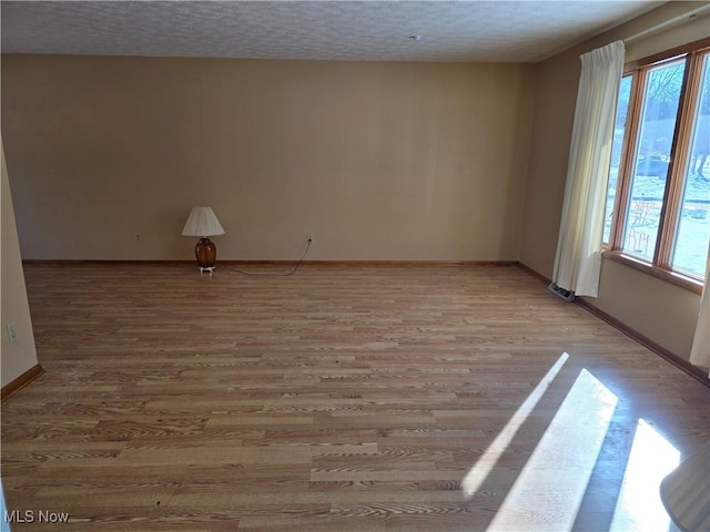 empty room with light wood-type flooring, a wealth of natural light, and a textured ceiling