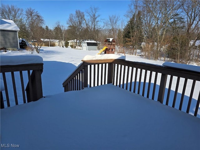 snow covered deck featuring a playground and a shed