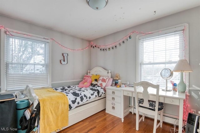 bedroom featuring hardwood / wood-style floors, baseboard heating, and multiple windows