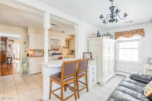 kitchen featuring a baseboard radiator, white cabinetry, ornate columns, and tile counters