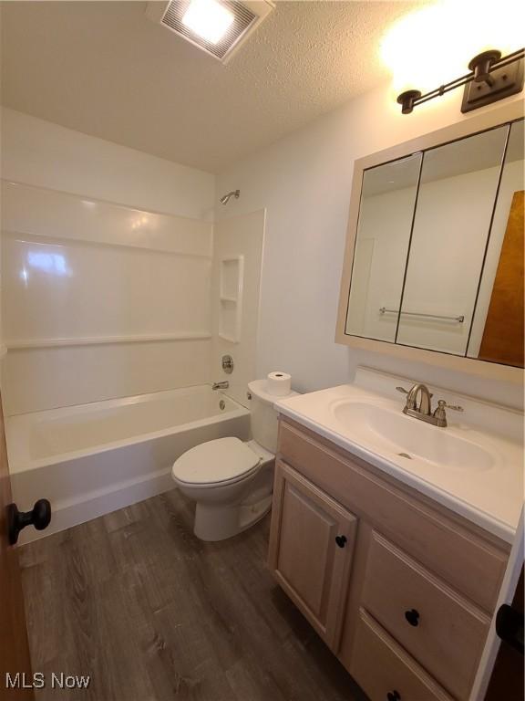 full bathroom with shower / washtub combination, hardwood / wood-style floors, toilet, a textured ceiling, and vanity