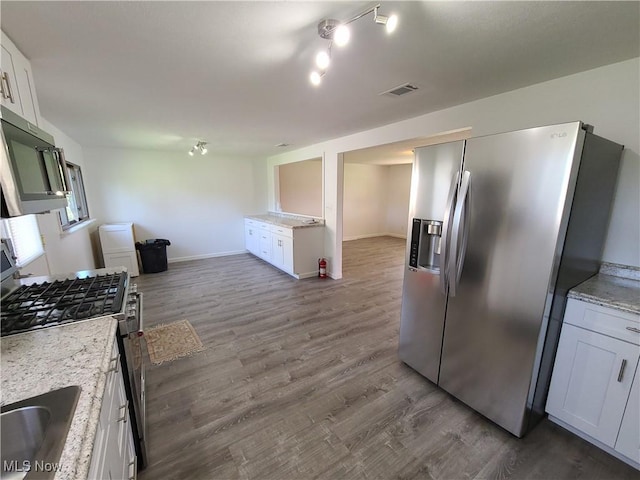 kitchen with light stone countertops, appliances with stainless steel finishes, hardwood / wood-style flooring, white cabinetry, and sink