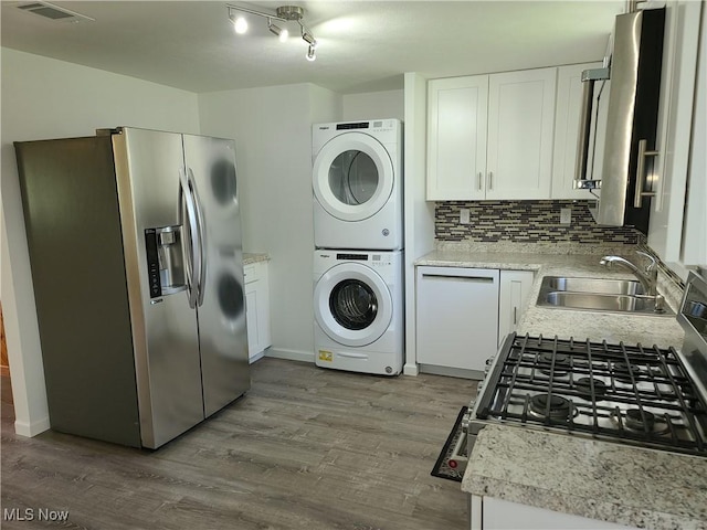 kitchen with stacked washer / dryer, appliances with stainless steel finishes, white cabinetry, sink, and backsplash