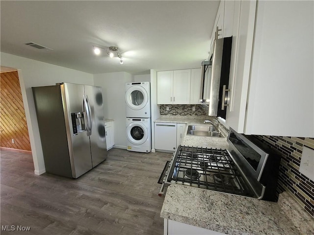 kitchen featuring sink, backsplash, white cabinets, stacked washer and clothes dryer, and stainless steel appliances