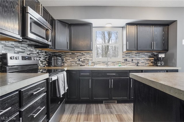 kitchen featuring sink, light wood-type flooring, decorative backsplash, and appliances with stainless steel finishes