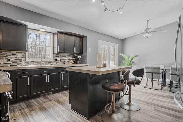 kitchen with sink, backsplash, a center island, a breakfast bar, and light hardwood / wood-style floors