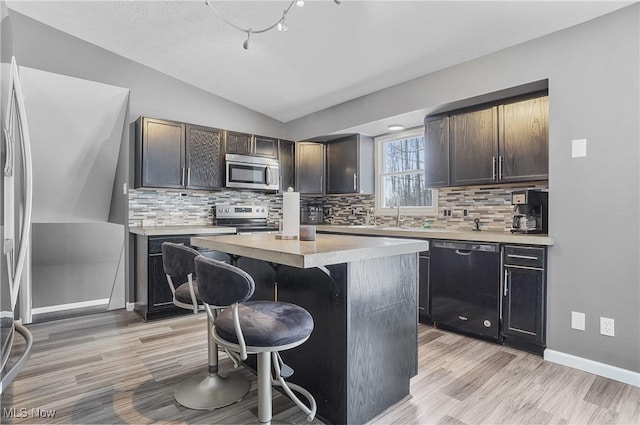 kitchen with lofted ceiling, a kitchen island, stainless steel appliances, a breakfast bar, and dark brown cabinets