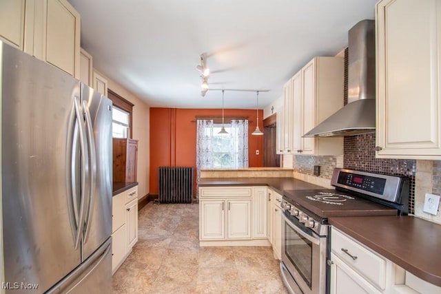 kitchen featuring radiator, wall chimney range hood, stainless steel appliances, tasteful backsplash, and rail lighting