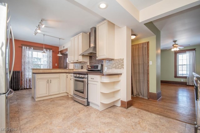 kitchen with appliances with stainless steel finishes, wall chimney exhaust hood, decorative light fixtures, kitchen peninsula, and cream cabinetry