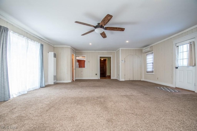 unfurnished living room featuring an AC wall unit, plenty of natural light, ornamental molding, and carpet flooring