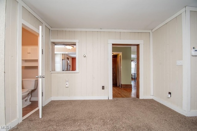 unfurnished bedroom featuring crown molding, light colored carpet, connected bathroom, and stainless steel refrigerator