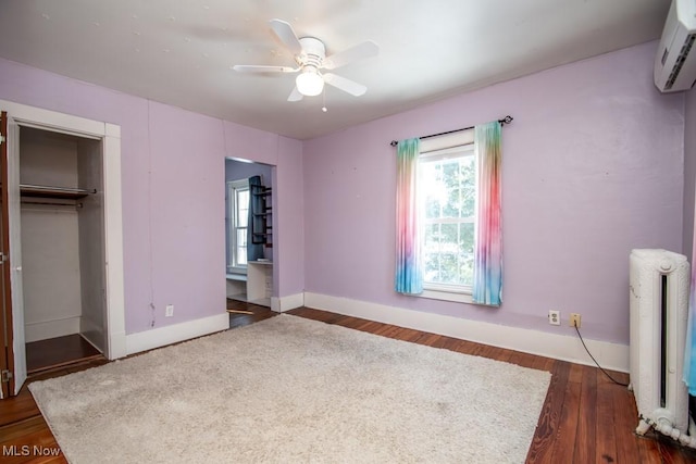 unfurnished bedroom featuring radiator heating unit, an AC wall unit, a closet, ceiling fan, and dark hardwood / wood-style floors