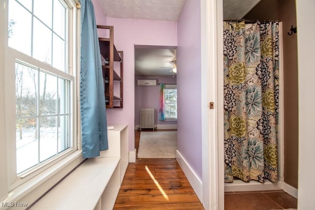 corridor with radiator heating unit, a healthy amount of sunlight, a wall mounted AC, and dark hardwood / wood-style flooring