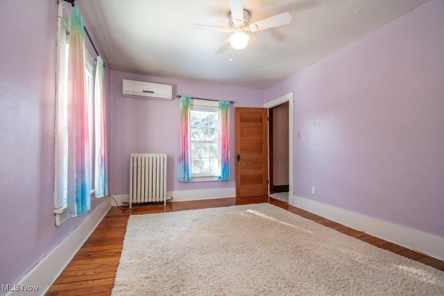 spare room featuring wood-type flooring, a wall mounted AC, radiator, and ceiling fan