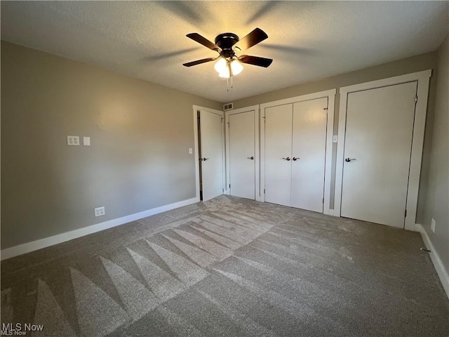 unfurnished bedroom featuring multiple closets, ceiling fan, a textured ceiling, and carpet floors