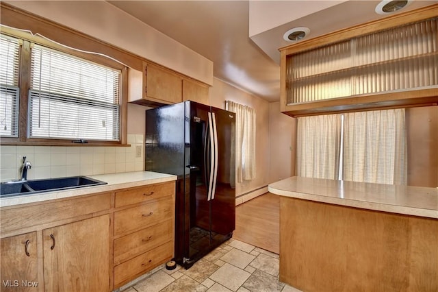 kitchen featuring sink, a baseboard radiator, black fridge, and tasteful backsplash