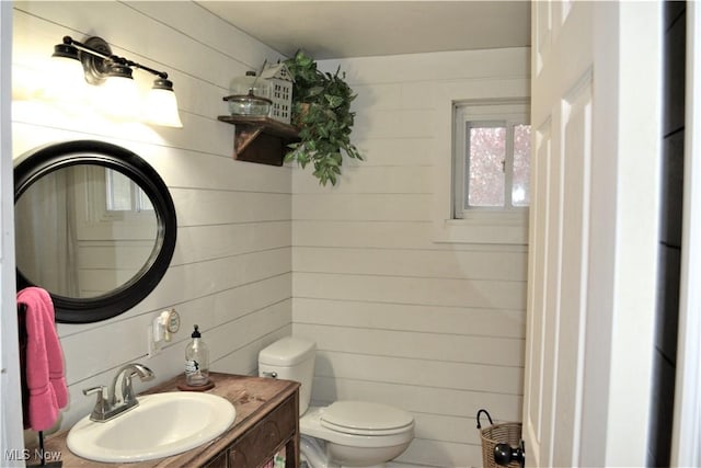 bathroom featuring toilet, vanity, and wooden walls