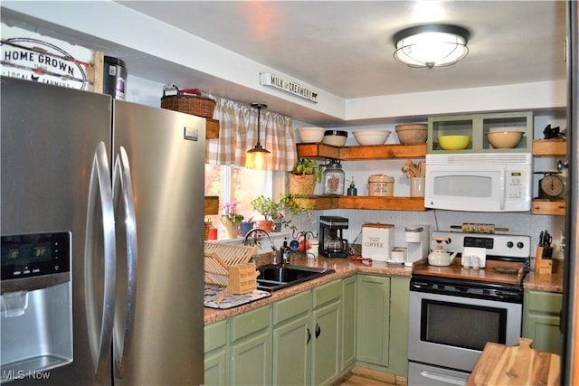 kitchen featuring light stone countertops, decorative light fixtures, stainless steel appliances, sink, and green cabinetry