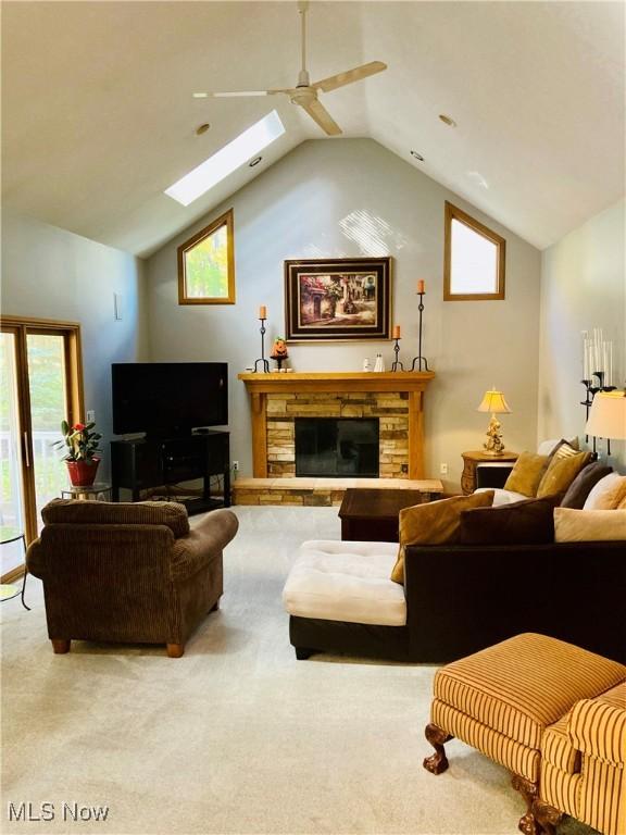 living room with a fireplace, lofted ceiling with skylight, ceiling fan, and carpet flooring