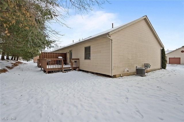 snow covered back of property with a wooden deck and central AC