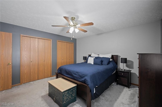 bedroom featuring ceiling fan, two closets, a textured ceiling, and carpet flooring