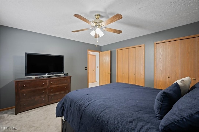 bedroom featuring ceiling fan, two closets, a textured ceiling, and light carpet