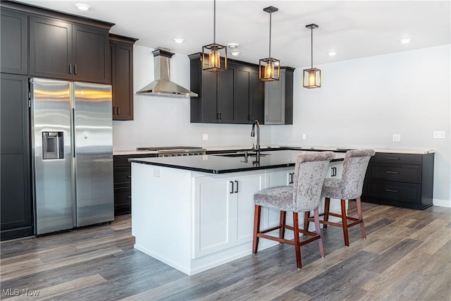 kitchen with pendant lighting, appliances with stainless steel finishes, wall chimney exhaust hood, an island with sink, and sink