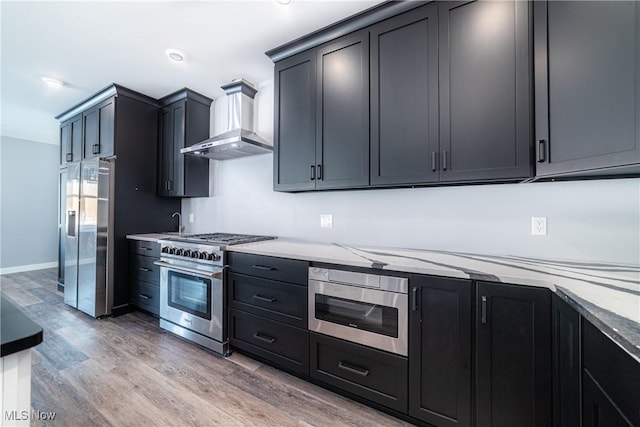 kitchen with hardwood / wood-style flooring, light stone countertops, wall chimney range hood, and appliances with stainless steel finishes