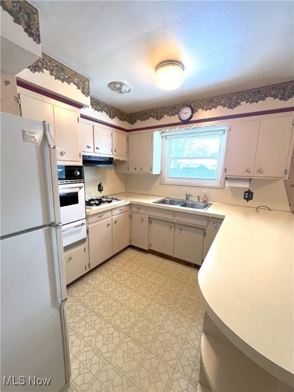 kitchen with sink, white appliances, a textured ceiling, and range hood