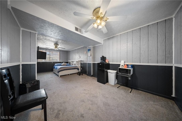 carpeted bedroom featuring ceiling fan, wood walls, and a textured ceiling