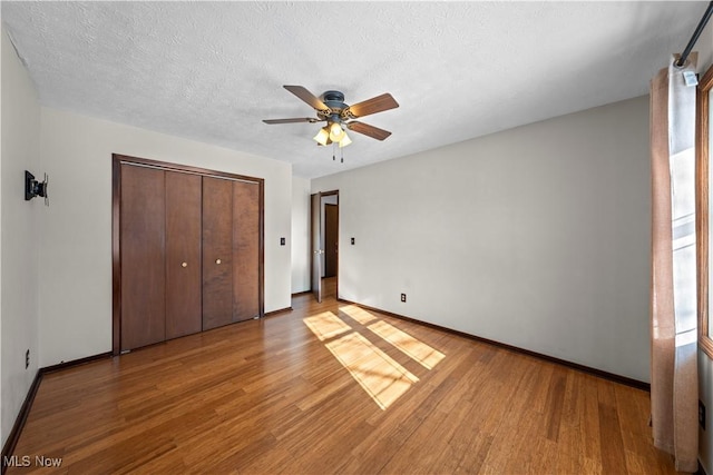 unfurnished bedroom with light wood-type flooring, a textured ceiling, a closet, and ceiling fan