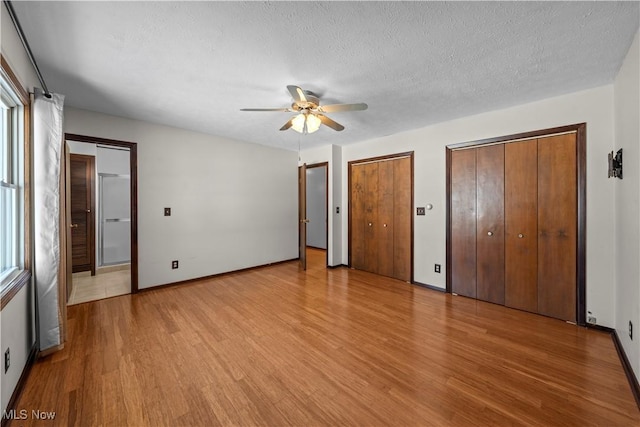 unfurnished bedroom with light wood-type flooring, ceiling fan, a textured ceiling, and two closets