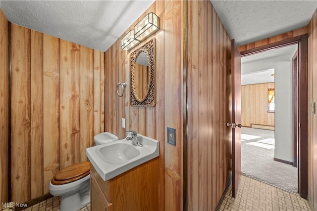 bathroom featuring wood walls, a textured ceiling, toilet, and vanity