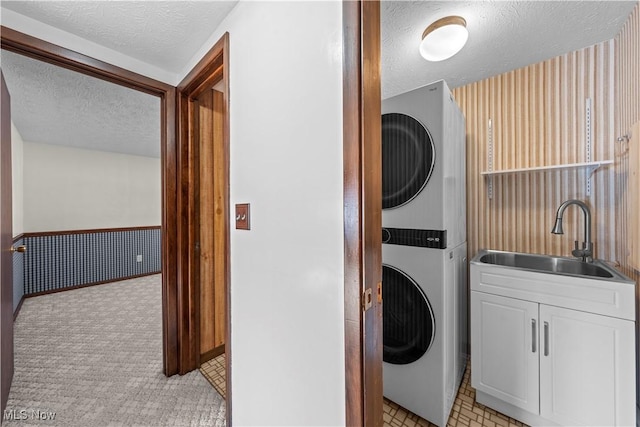 washroom with sink, stacked washer and clothes dryer, a textured ceiling, and cabinets