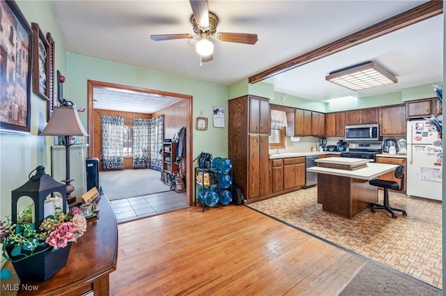 kitchen featuring light wood-type flooring, appliances with stainless steel finishes, a kitchen breakfast bar, a kitchen island, and ceiling fan