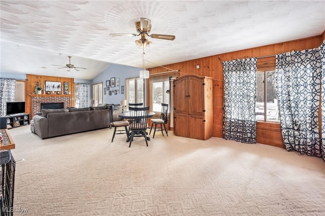 carpeted living room featuring wooden walls, lofted ceiling, ceiling fan, a brick fireplace, and a textured ceiling