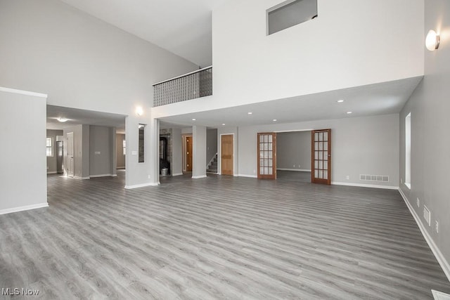 unfurnished living room featuring light hardwood / wood-style floors, a high ceiling, and french doors